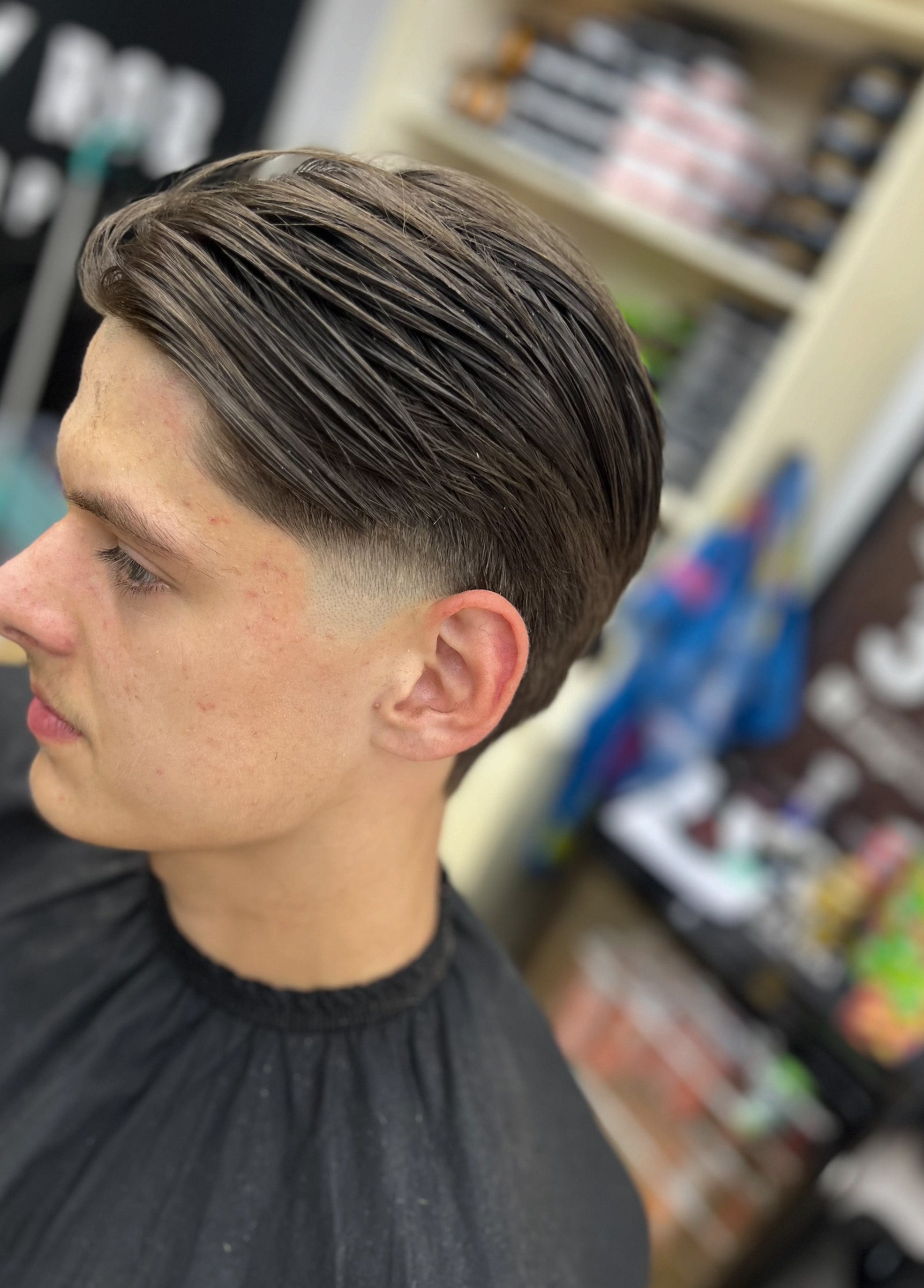 Achterover gekamd haar met een lage fade, de kast met producten op de achtergrond